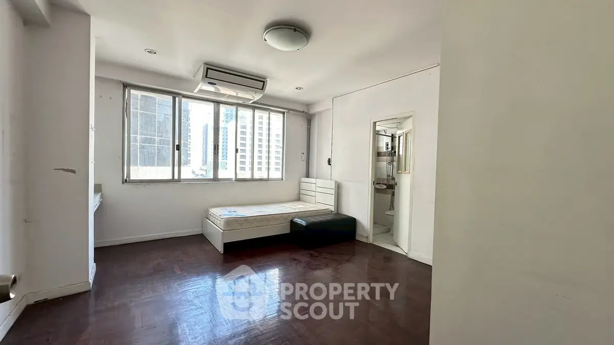 Spacious bedroom with large windows and city view, featuring a minimalist design and hardwood floors.