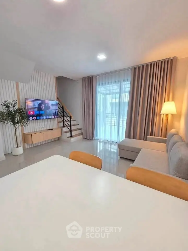 Modern living room with stylish decor and natural light, featuring a cozy sofa and elegant staircase.