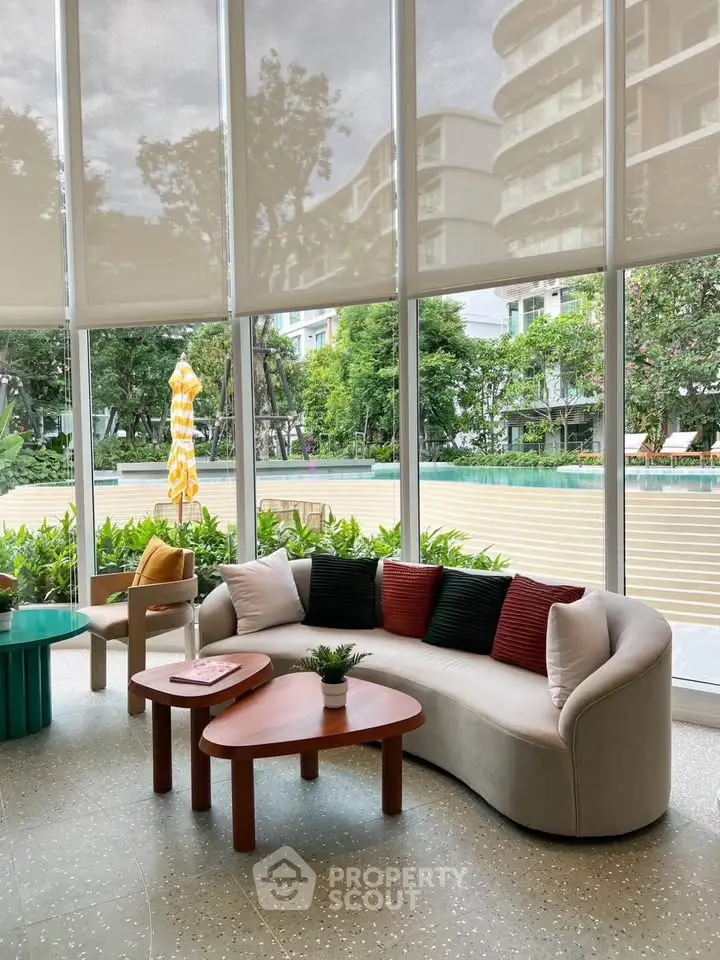 Modern living room with large windows overlooking lush garden and pool area.