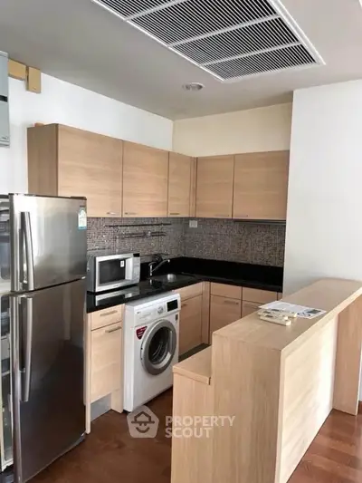 Modern kitchen with wooden cabinets, stainless steel fridge, and washing machine