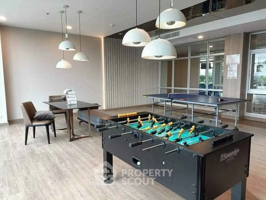 Modern recreational room with foosball and ping pong tables, stylish lighting, and wooden flooring.