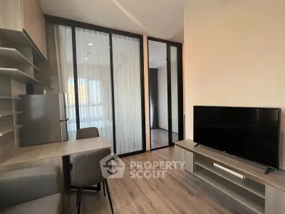 Modern living room with sleek furniture and glass partition, featuring a flat-screen TV and dining area.