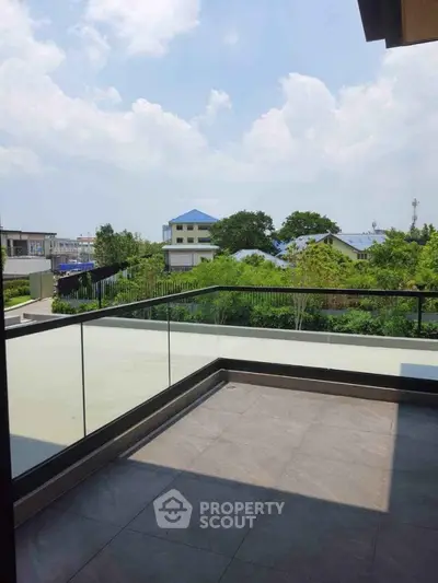 Spacious balcony with glass railing offering scenic views of lush greenery and blue skies.