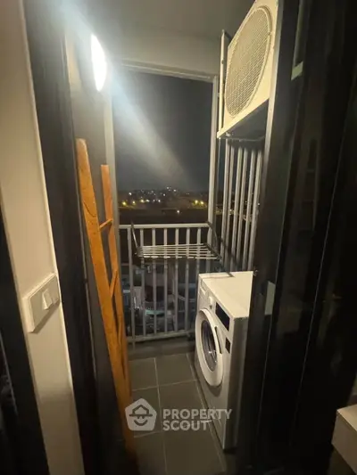 Compact balcony with washing machine and city view at night, ideal for urban living.