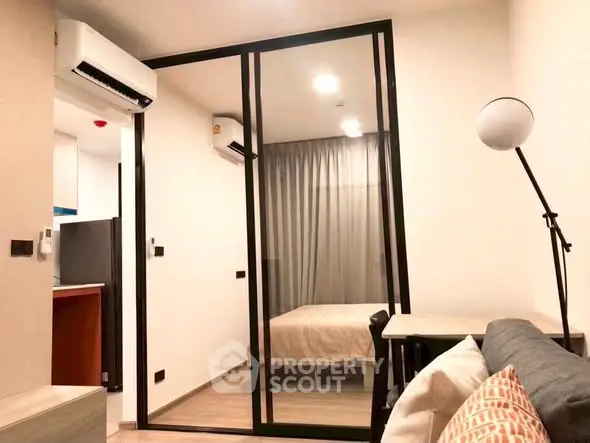 Modern apartment interior with cozy living room and bedroom separated by glass partition.