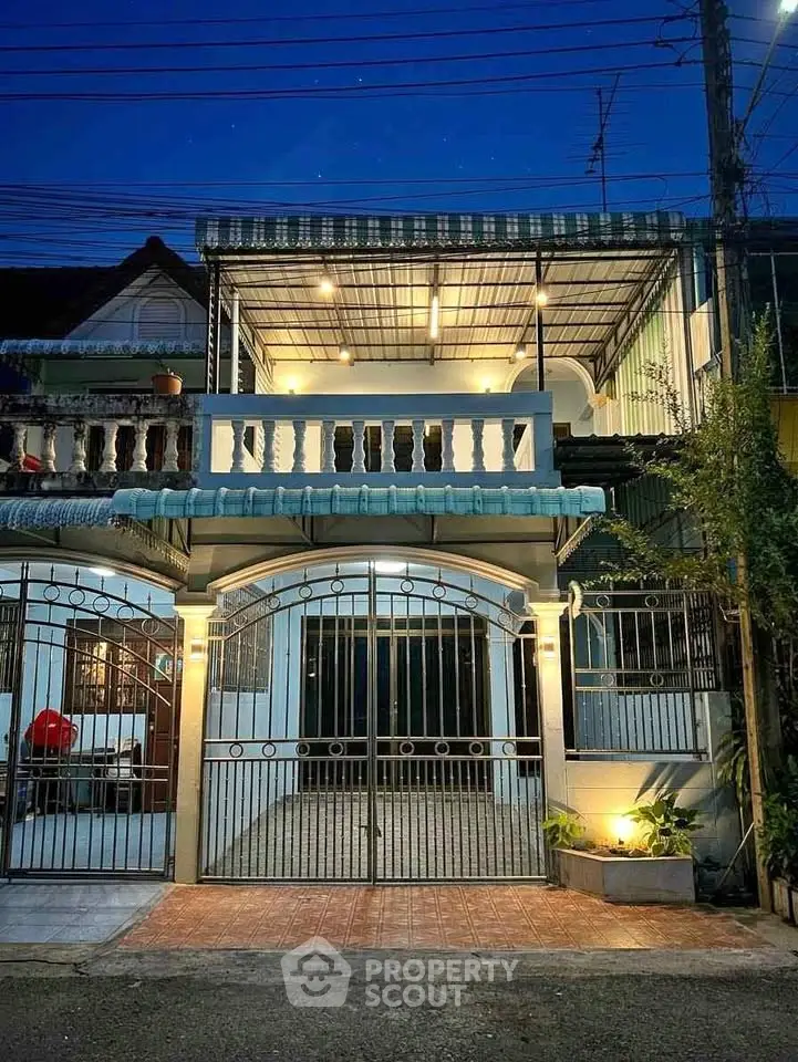 Charming two-story house with gated entrance and balcony, beautifully lit at dusk.