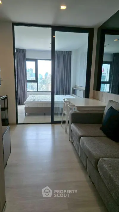 Modern apartment with open living area and bedroom, featuring city views through large windows.