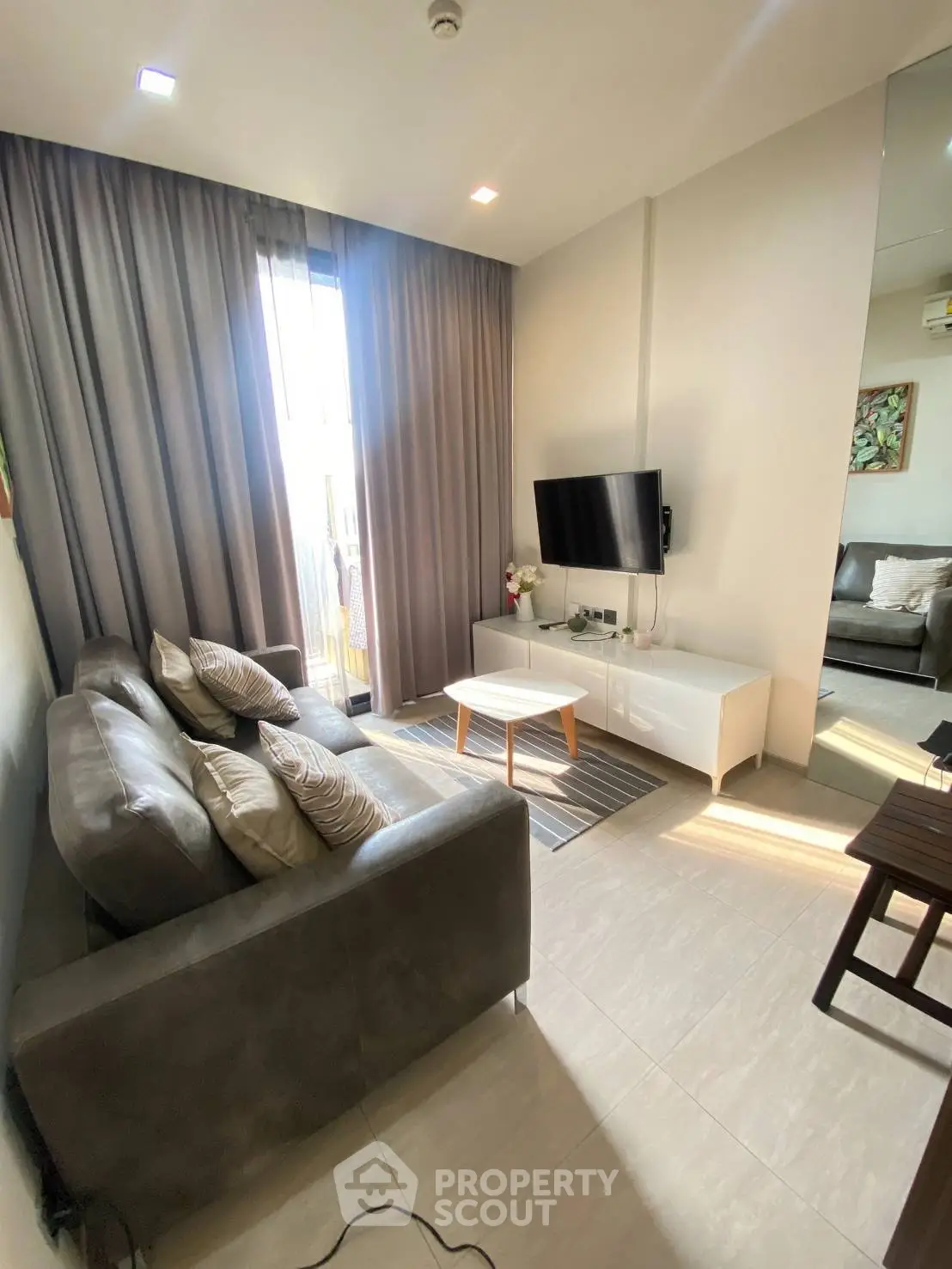 Modern living room with cozy sofa, wall-mounted TV, and natural light from large window.