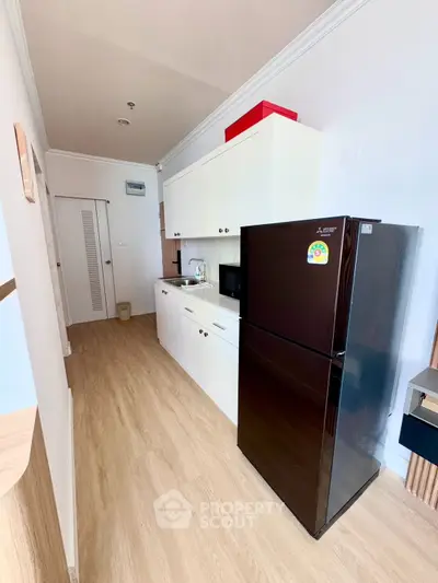 Modern kitchen with sleek black fridge and white cabinetry in a cozy apartment.