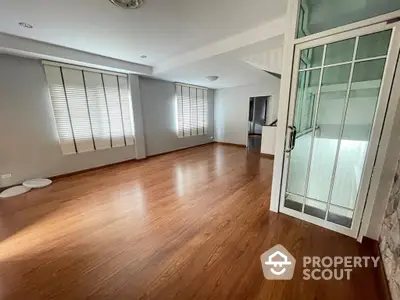 Spacious living room with gleaming hardwood floors, ample natural light, and modern glass doors leading to another room.