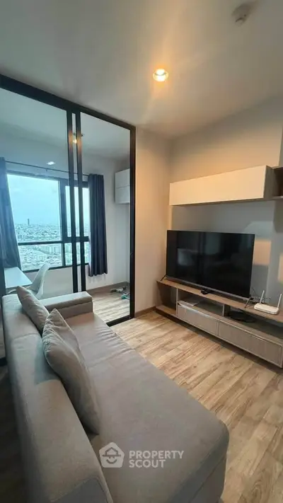 Modern living room with large TV and city view from balcony, featuring sleek furniture and wooden flooring.