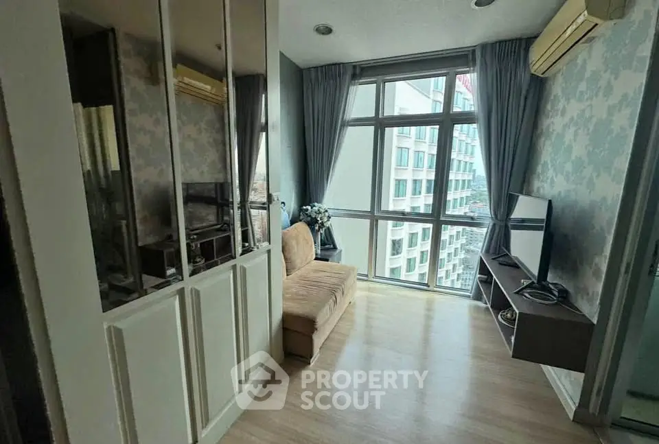 Modern living room with large windows and city view, featuring a cozy sofa and wall-mounted TV.
