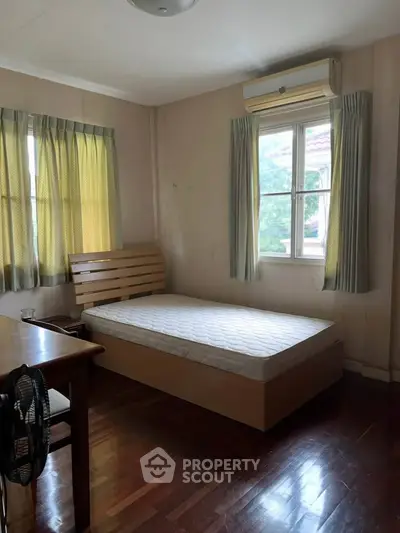 Cozy bedroom with wooden flooring and natural light, featuring a single bed and air conditioning.