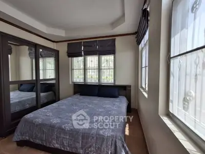 Cozy bedroom with large windows and mirrored wardrobe in a well-lit space.