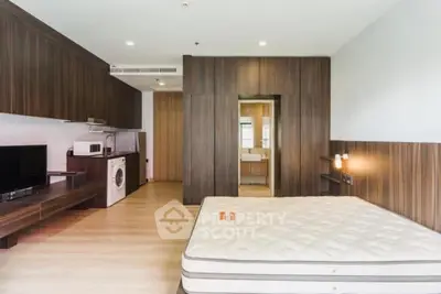 Modern studio apartment with wooden accents, featuring a bed, TV, and compact kitchen with washing machine.
