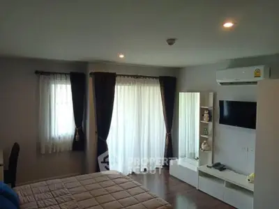 Cozy bedroom with modern decor, featuring a wall-mounted TV and large windows with curtains.