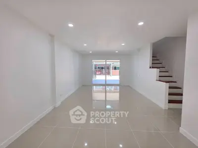 Spacious modern living room with glossy tiled floors and staircase, perfect for family gatherings.