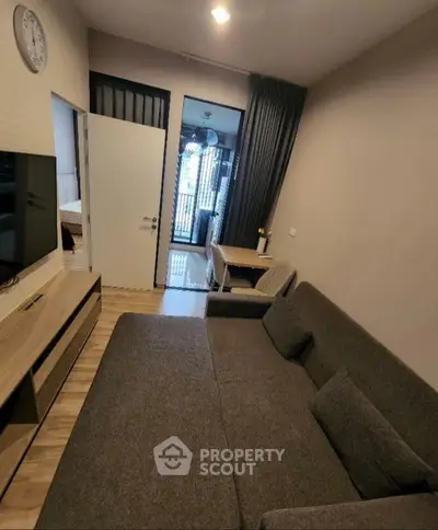 Modern living room with cozy sofa and wall-mounted TV, leading to a bright balcony view.