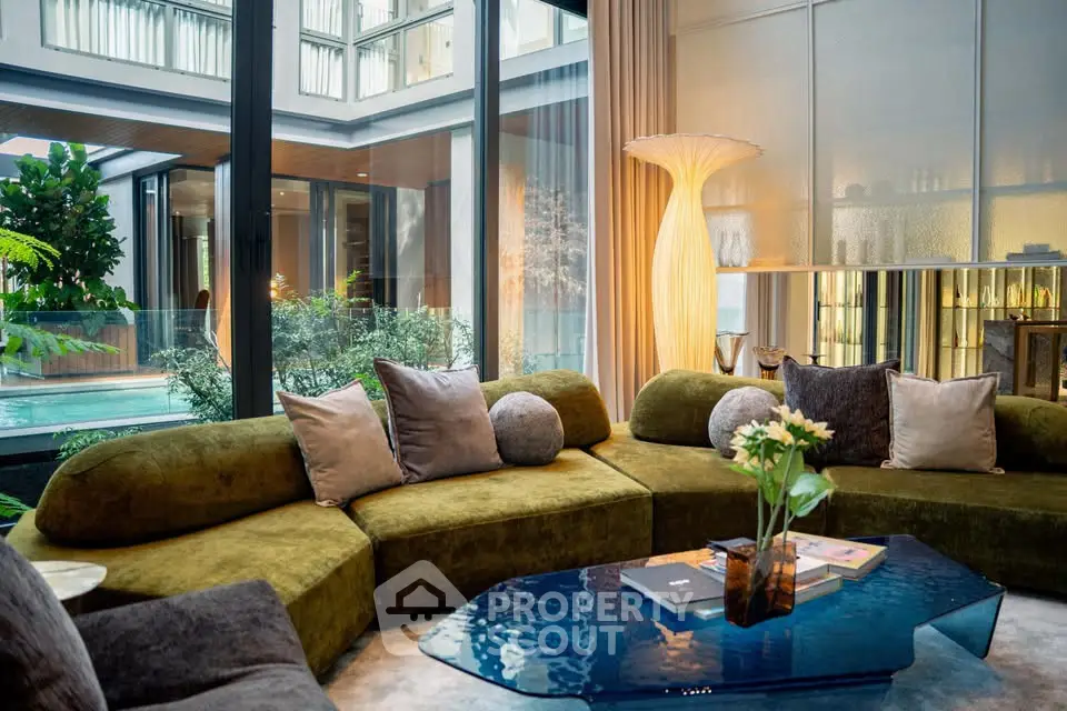 Luxurious living room with plush green sofa and glass coffee table overlooking a serene garden view.