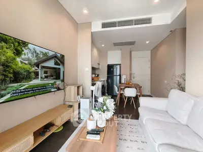 Modern living room with sleek furniture and large TV, open layout to dining area and kitchen.