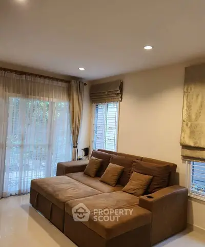 Spacious living room with large brown sofa and natural light from windows.