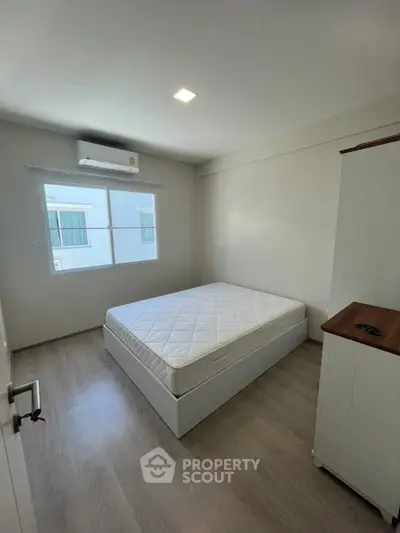 Spacious bedroom with natural light, featuring a comfortable bed and modern air conditioning unit.