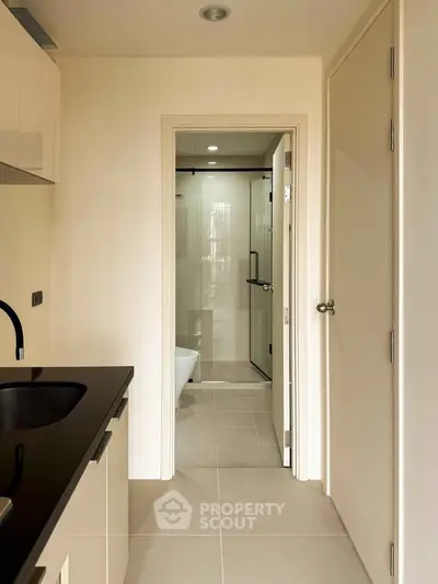 Modern apartment interior with sleek kitchen and view into stylish bathroom.