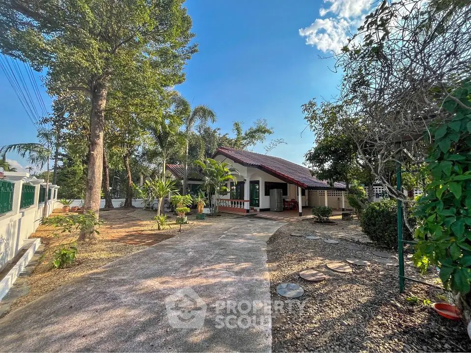 Charming single-story home nestled among mature trees with a spacious driveway and welcoming front porch, offering a serene suburban retreat.