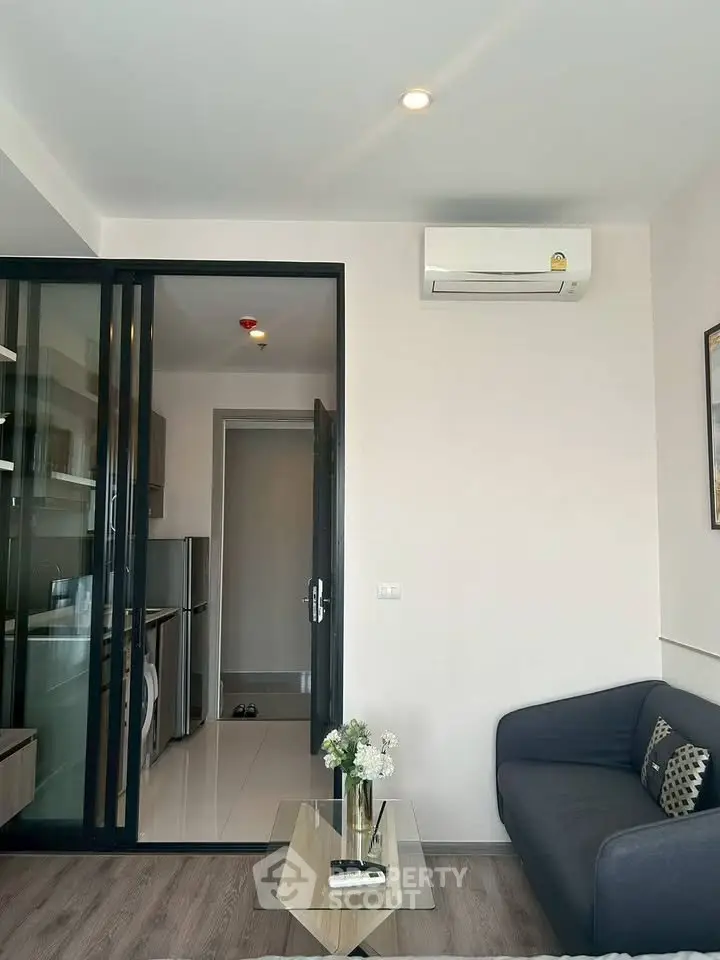 Modern living room with sleek design and air conditioning, adjacent to a compact kitchen with glass sliding doors.