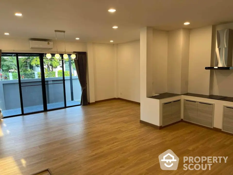 Spacious open-plan living area with modern kitchen, ample natural light, and a view of greenery through large balcony doors, perfect for entertaining and relaxation.