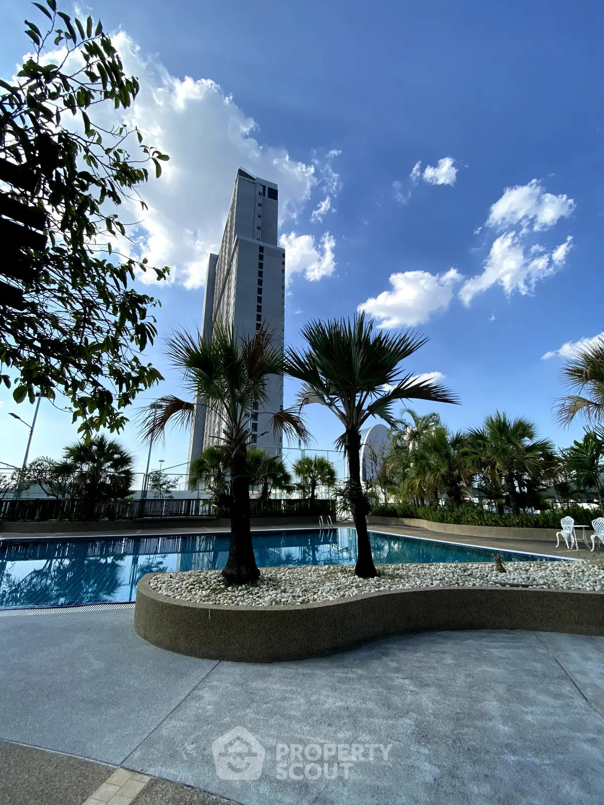 Luxurious high-rise building with serene pool and palm trees under a clear blue sky.