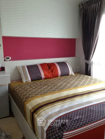 Cozy bedroom with a large bed adorned with stylish linens, a bold red accent wall, and elegant drapery, offering a warm and inviting atmosphere.