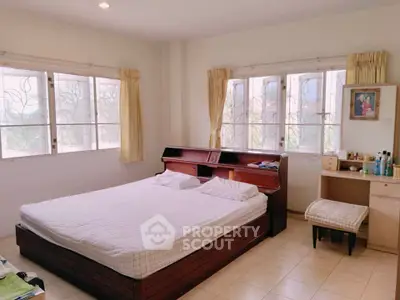 Spacious bedroom with large windows and natural light, featuring a cozy bed and a small vanity area.