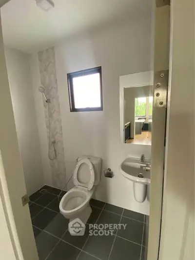 Modern bathroom with sleek design, featuring a toilet, sink, and shower area with natural light.