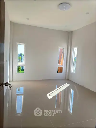 Spacious empty room with glossy tiled floor and large windows for natural light.