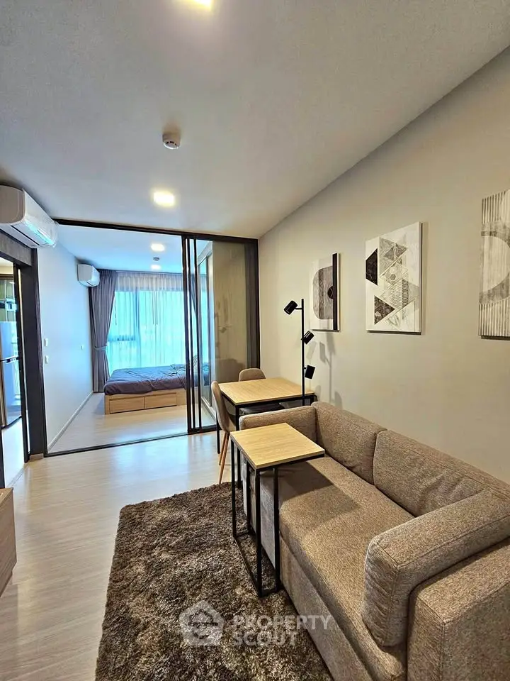 Modern living room with cozy sofa and stylish decor leading to a bedroom with natural light.
