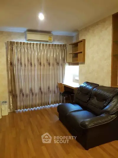 Cozy living room with leather sofa and wooden flooring, featuring elegant curtains and a compact workspace.