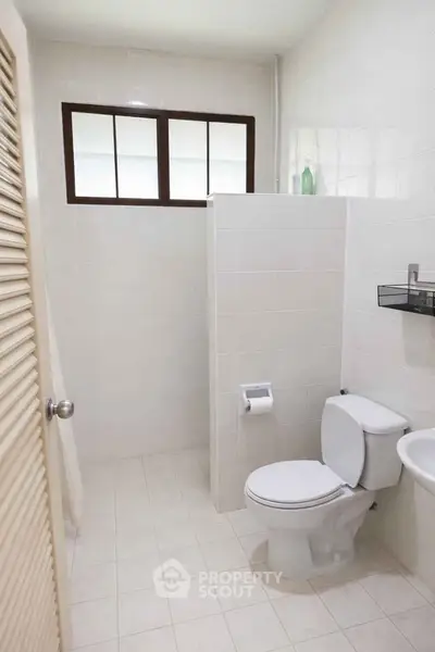 Modern bathroom with white tiles and window, featuring toilet and sink.