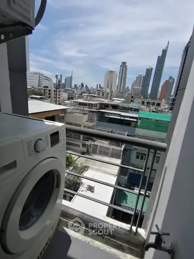 City view from balcony with washing machine, showcasing urban skyline.