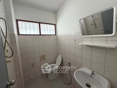 Simple bathroom with tiled walls, toilet, sink, and mirror, ideal for renovation.