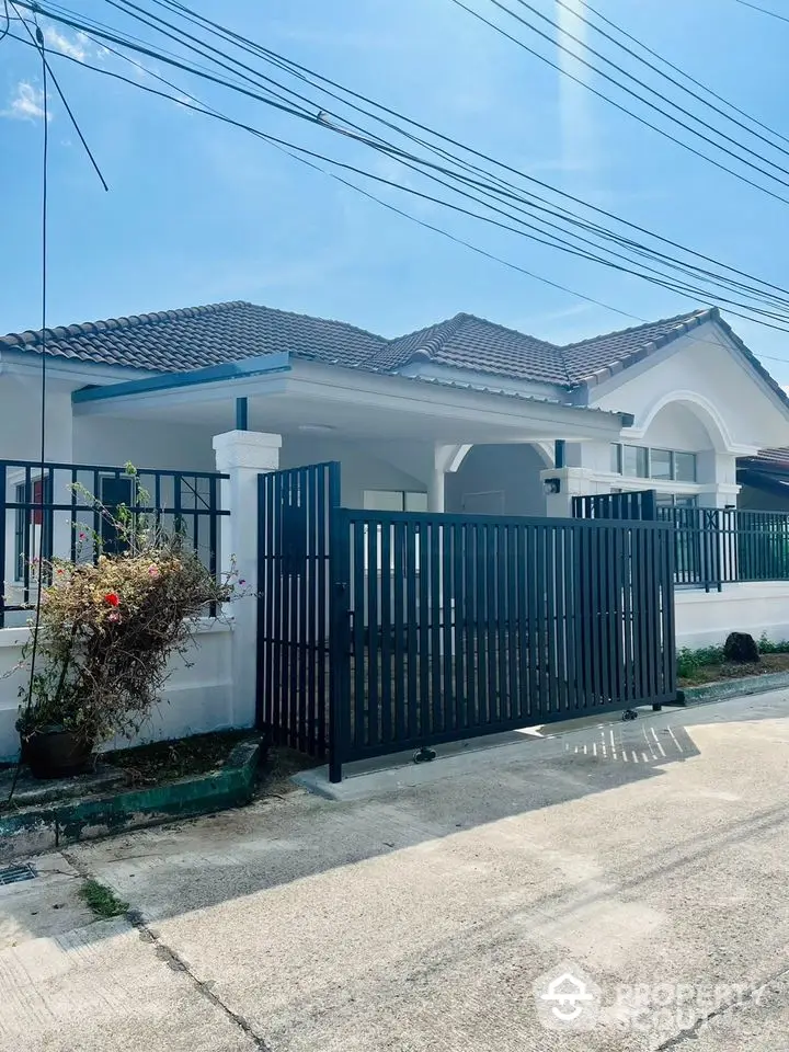 Charming single-story home with a spacious driveway, elegant blue-tiled roof, and secure black gate, nestled in a serene neighborhood.