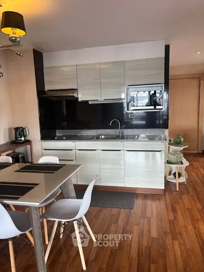 Modern kitchen with sleek cabinetry and dining area, featuring wooden flooring and contemporary design.
