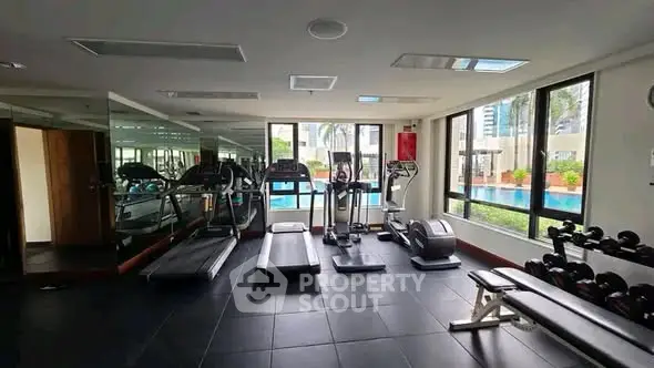 Spacious gym with modern equipment and pool view in luxury apartment complex.