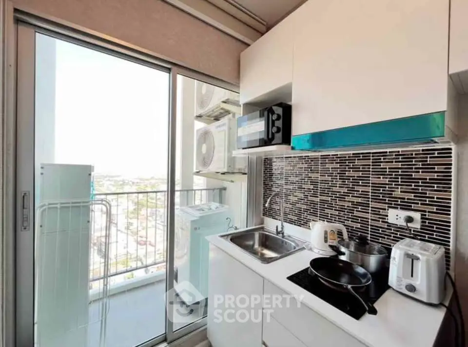 Modern compact kitchen with balcony view, featuring sleek appliances and stylish backsplash.