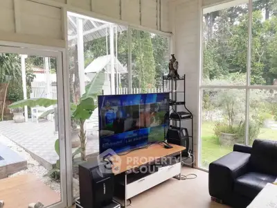 Bright living room with large windows overlooking a lush garden, featuring modern furniture and a flat-screen TV.