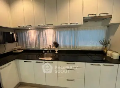 Modern kitchen with sleek white cabinets and black countertops, featuring an electric stove and elegant decor.