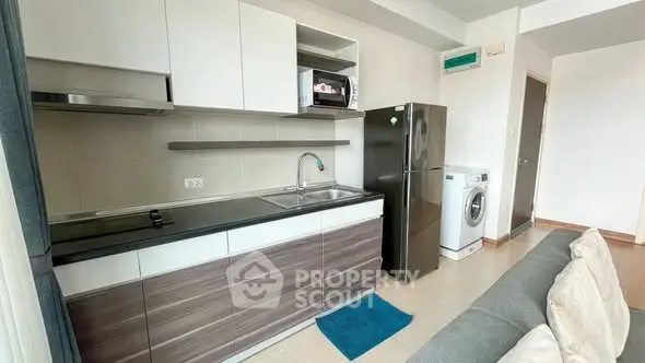 Modern kitchen with sleek cabinets, stainless steel fridge, and washing machine in cozy apartment.