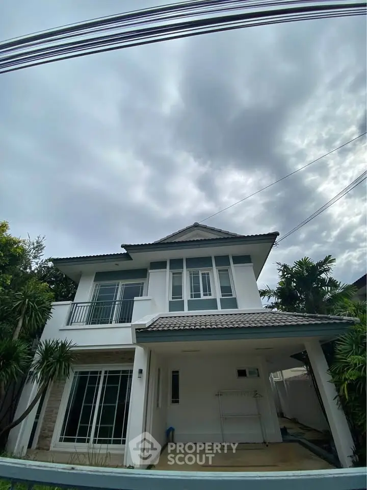 Modern two-story house with sleek design and lush greenery under a cloudy sky.