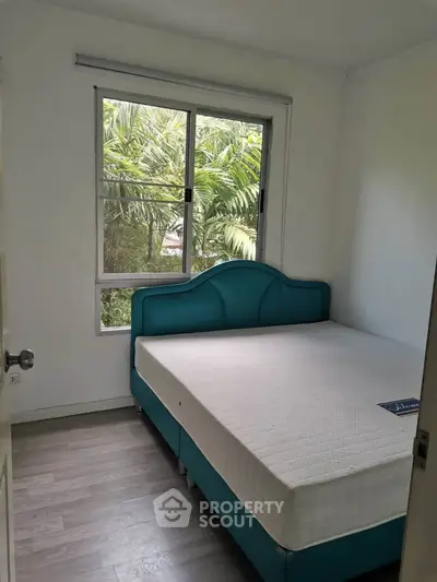 Cozy bedroom with large window and lush greenery view, featuring a stylish bed and sleek flooring.
