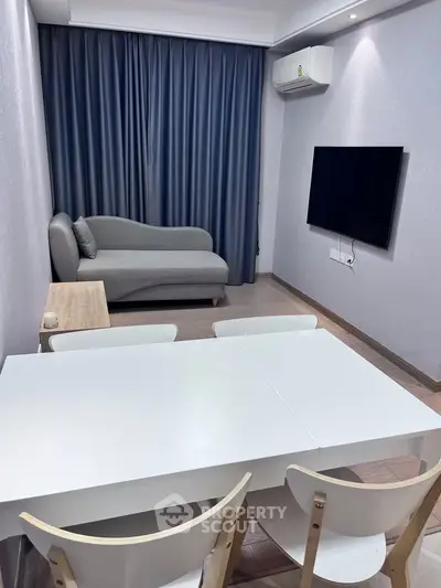 Modern living room with sleek furniture and wall-mounted TV, featuring a cozy gray sofa and elegant dining area.